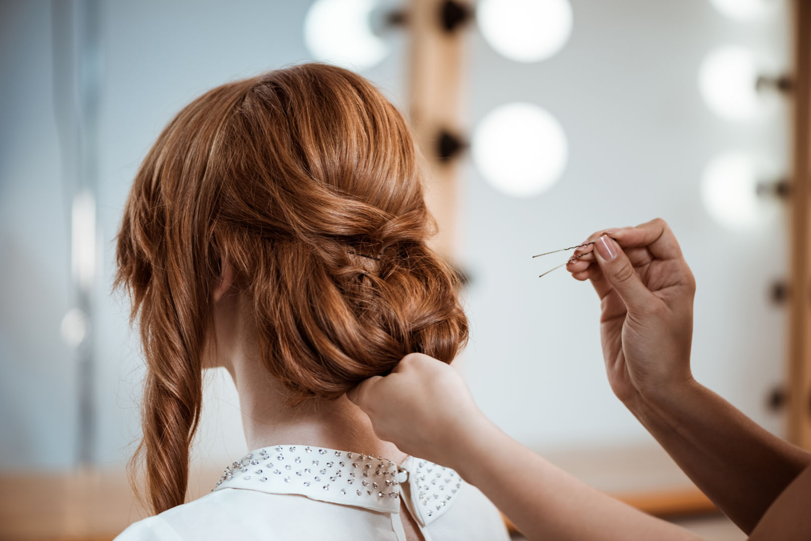 Female hairdresser making hairstyle to redhead girl in beauty salon.