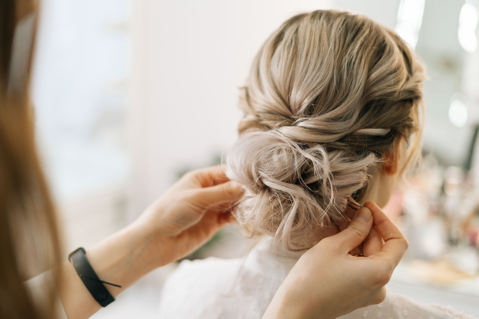 Close up of hands of hairdresser making hairstyle young blonde woman in beauty salon.