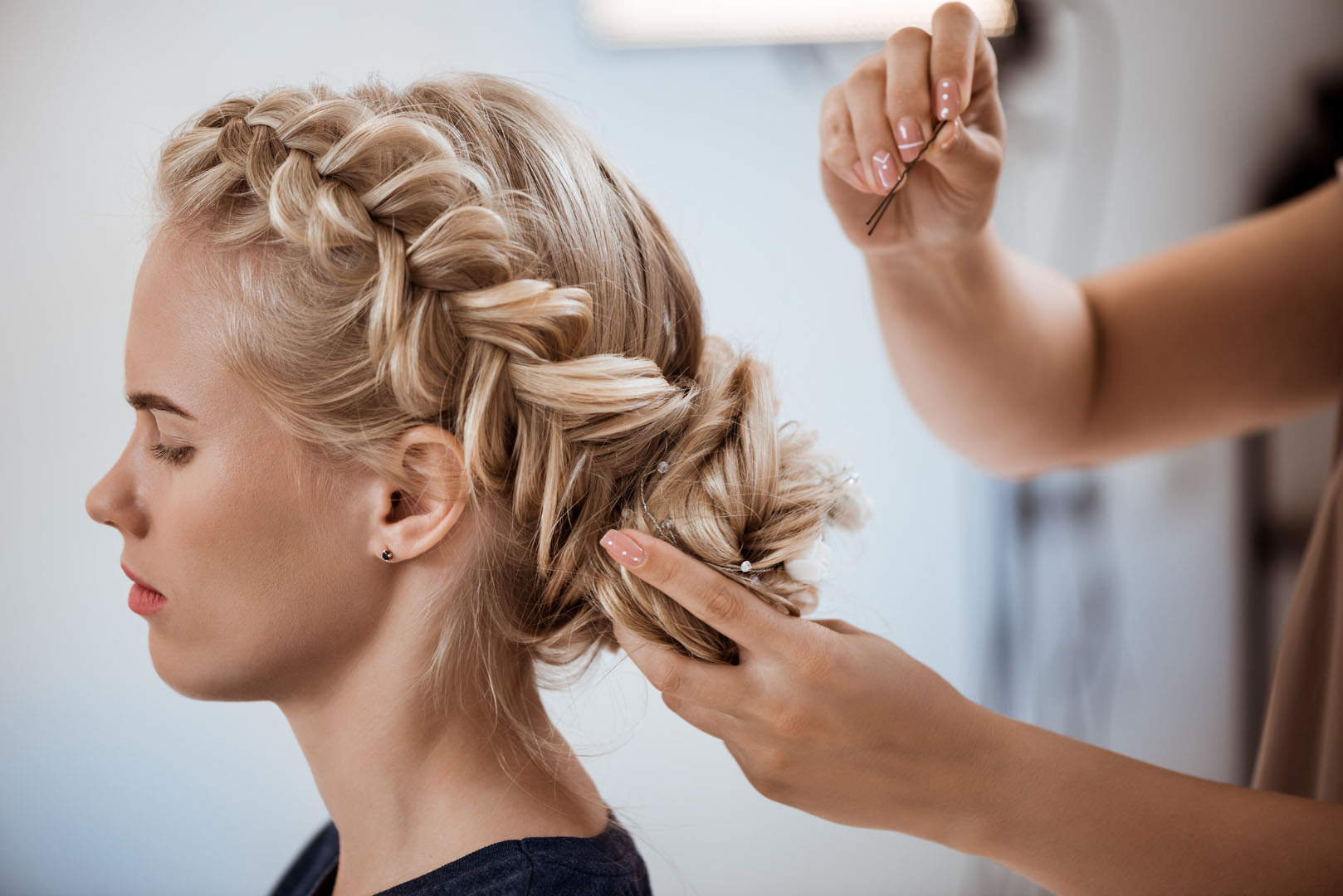 Female hairdresser making hairstyle to blonde girl in beauty salon.